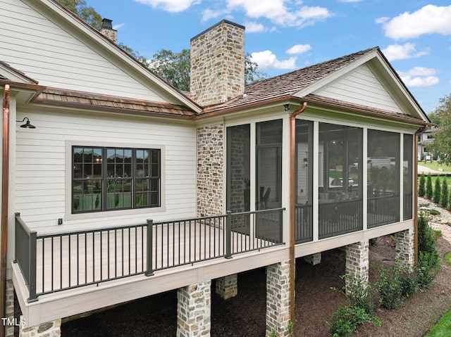back of property with a sunroom, a chimney, and a deck