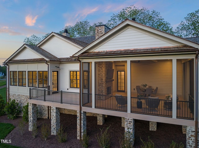 back of house at dusk with a chimney and a sunroom
