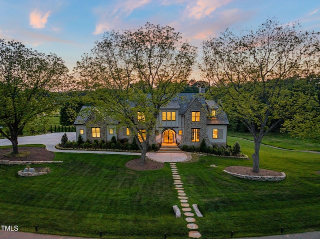 view of front of property featuring curved driveway, a chimney, stone siding, and a front yard