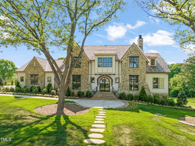 tudor home featuring stone siding, a front lawn, and a chimney