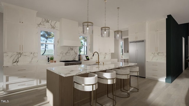 kitchen featuring an island with sink, decorative light fixtures, stainless steel built in fridge, white cabinetry, and a sink