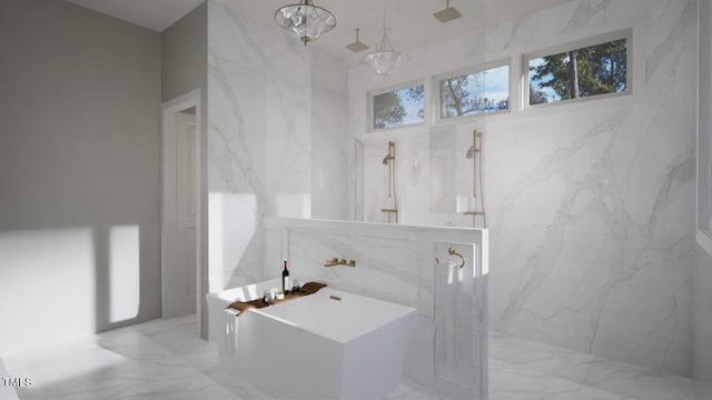 bathroom featuring marble finish floor, a marble finish shower, an inviting chandelier, a freestanding tub, and stone wall