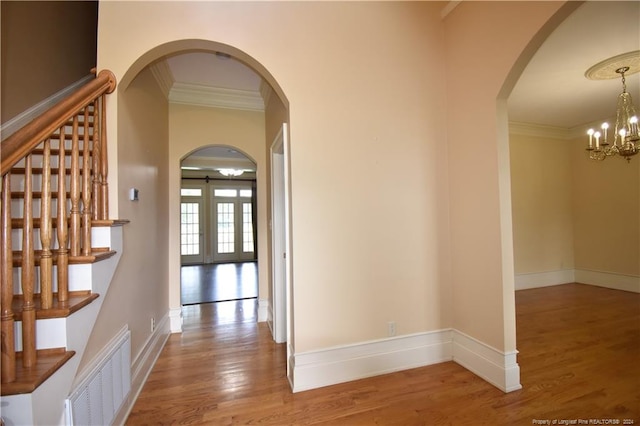 corridor featuring french doors, hardwood / wood-style floors, a notable chandelier, and ornamental molding