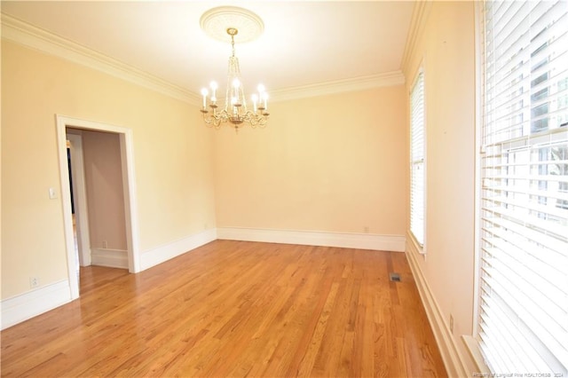 spare room featuring a healthy amount of sunlight, hardwood / wood-style floors, a chandelier, and ornamental molding