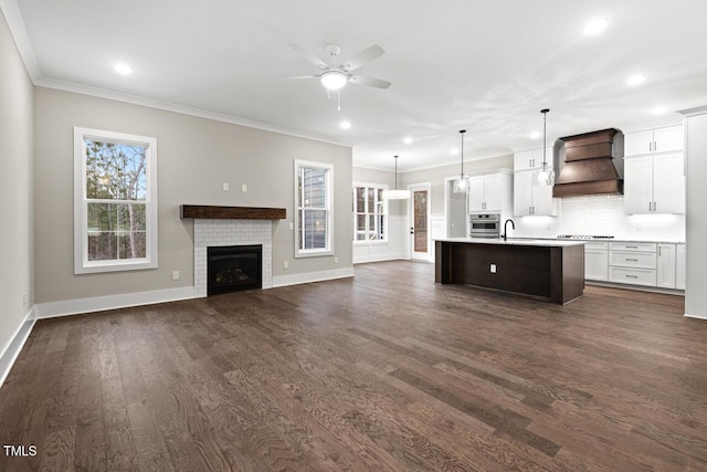 kitchen with sink, custom exhaust hood, tasteful backsplash, decorative light fixtures, and a kitchen island with sink