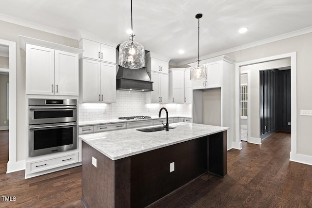 kitchen with light stone countertops, a kitchen island with sink, white cabinets, and appliances with stainless steel finishes