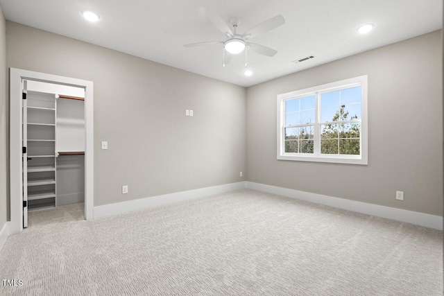 unfurnished bedroom featuring a walk in closet, light colored carpet, ceiling fan, and a closet