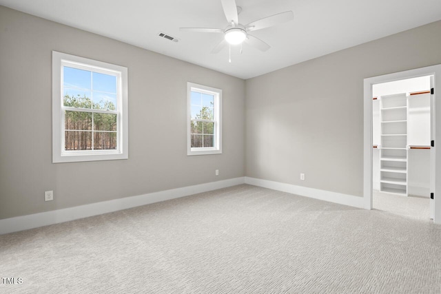 unfurnished bedroom featuring a spacious closet, a closet, ceiling fan, and carpet