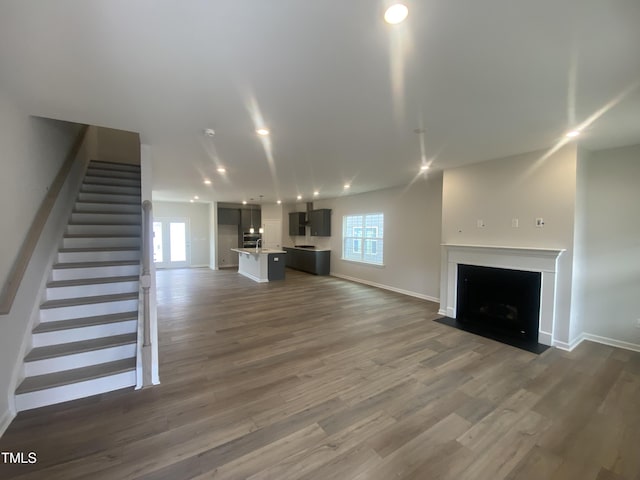 unfurnished living room featuring a fireplace with flush hearth, stairway, wood finished floors, and recessed lighting