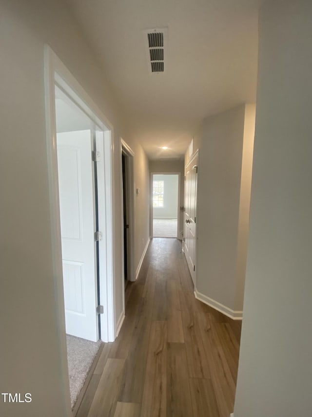 hall featuring baseboards, visible vents, and wood finished floors