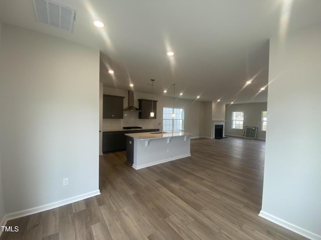 kitchen featuring light countertops, visible vents, open floor plan, a sink, and wall chimney exhaust hood