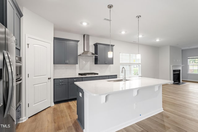 9249 Kitchin Farms Way Unit 432, Wake Forest, NC 27587 - kitchen with wall chimney exhaust hood, a sink, light wood-type flooring, light countertops, and a center island with sink