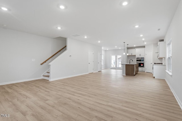 unfurnished living room with recessed lighting, a sink, baseboards, stairs, and light wood finished floors