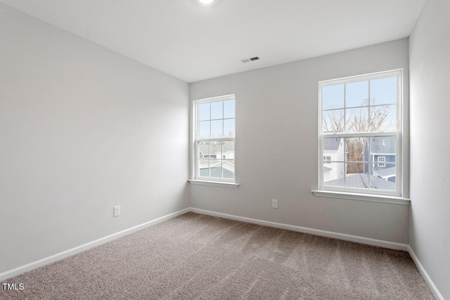 carpeted empty room featuring baseboards, visible vents, and a healthy amount of sunlight