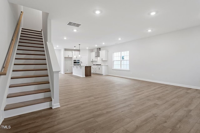 unfurnished living room with recessed lighting, visible vents, stairway, light wood-type flooring, and baseboards