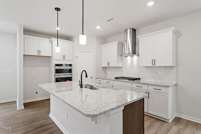 kitchen featuring stainless steel appliances, a sink, visible vents, wall chimney range hood, and decorative backsplash