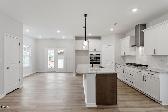 kitchen featuring light stone counters, a sink, light wood-style floors, wall chimney range hood, and backsplash