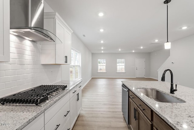 kitchen featuring a healthy amount of sunlight, wall chimney exhaust hood, stainless steel appliances, and a sink