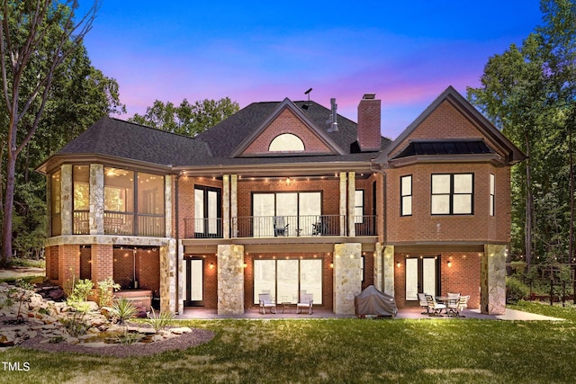 back house at dusk with a yard, a patio, and a balcony