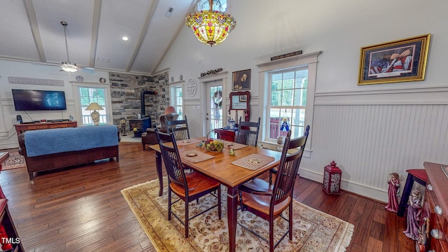 dining area with high vaulted ceiling, ceiling fan with notable chandelier, dark hardwood / wood-style flooring, and a wood stove