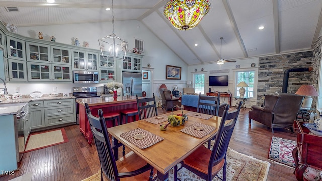 dining room featuring a wood stove, ceiling fan with notable chandelier, dark hardwood / wood-style floors, sink, and high vaulted ceiling