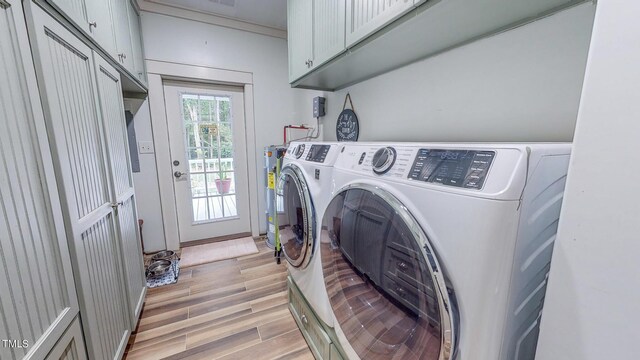 laundry area with electric water heater, washer and clothes dryer, light wood-type flooring, and cabinets