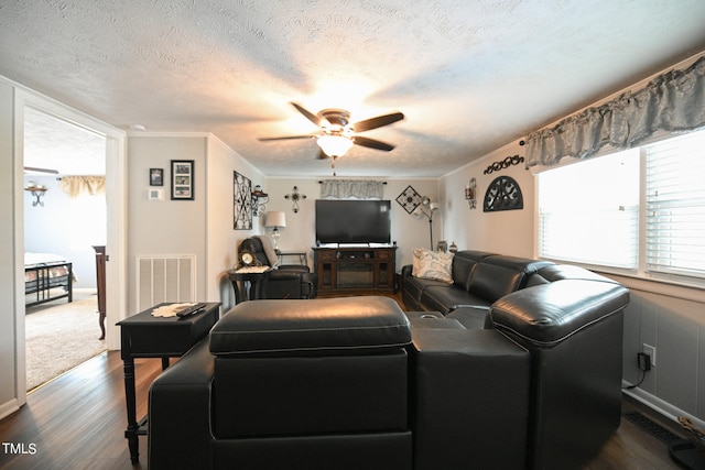 living room featuring ceiling fan, ornamental molding, dark wood-type flooring, and a textured ceiling