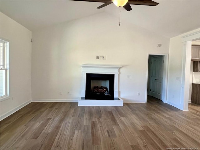 unfurnished living room featuring a fireplace with raised hearth, baseboards, lofted ceiling, wood finished floors, and a ceiling fan