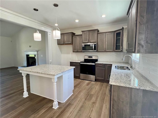 kitchen with wood finished floors, a fireplace, a sink, appliances with stainless steel finishes, and tasteful backsplash