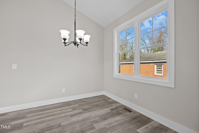 unfurnished dining area with lofted ceiling, wood-type flooring, and a chandelier