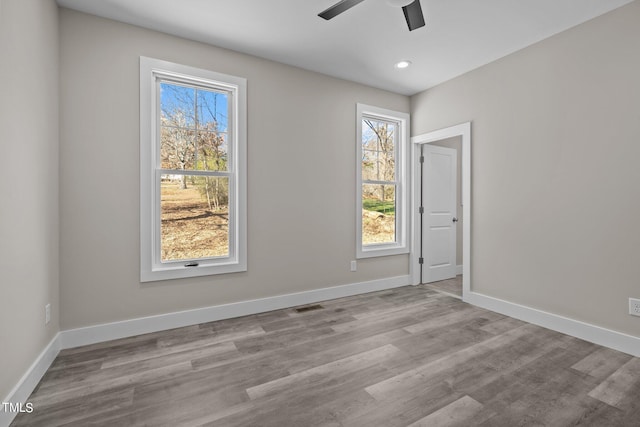 empty room with a healthy amount of sunlight, ceiling fan, and light hardwood / wood-style flooring