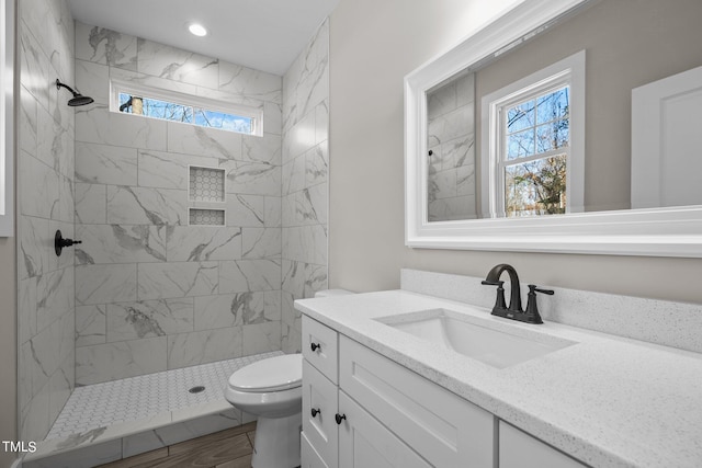 bathroom with tiled shower, vanity, toilet, and plenty of natural light