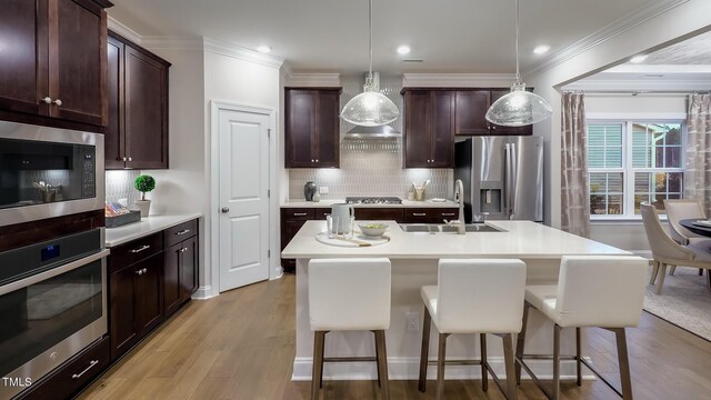 kitchen with pendant lighting, stainless steel appliances, a kitchen breakfast bar, and a center island with sink