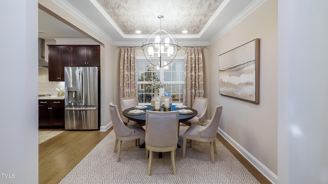 dining room featuring a chandelier, light wood-type flooring, a raised ceiling, and ornamental molding