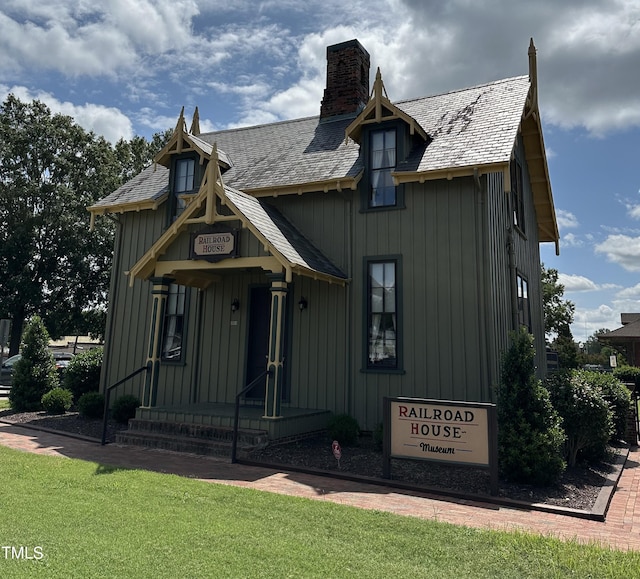 view of front of home with board and batten siding, entry steps, a chimney, and a front lawn