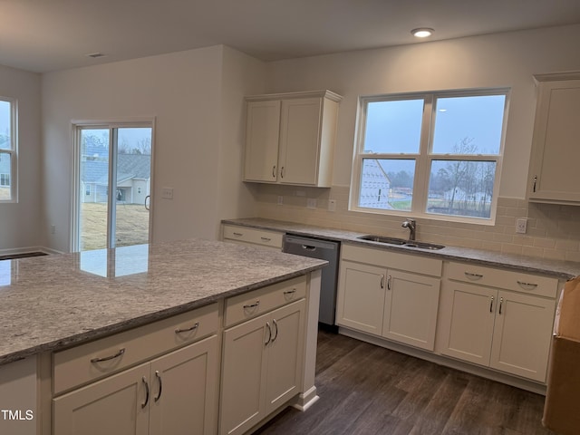 kitchen with dark wood-style floors, light stone counters, stainless steel dishwasher, white cabinetry, and a sink