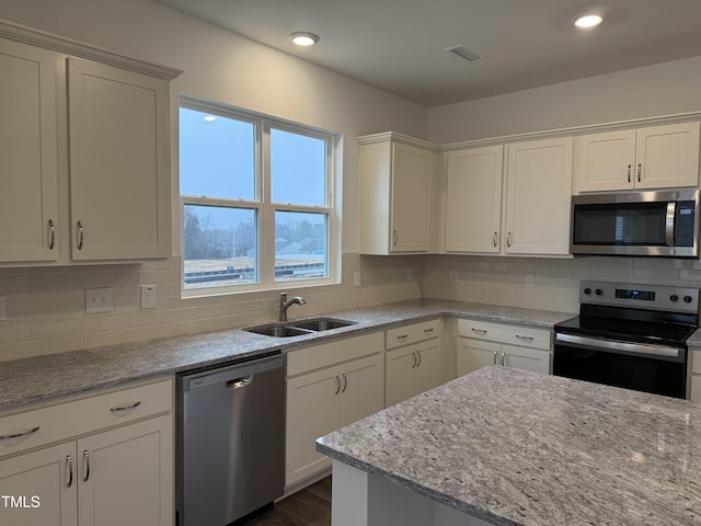 kitchen with light stone countertops, white cabinetry, appliances with stainless steel finishes, and a sink