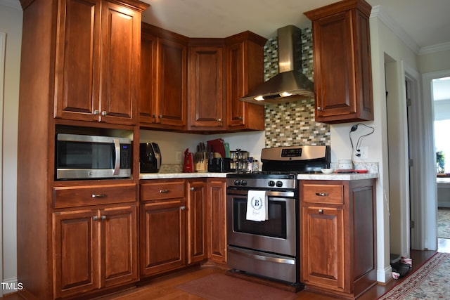 kitchen featuring crown molding, dark wood-type flooring, light stone countertops, wall chimney exhaust hood, and appliances with stainless steel finishes