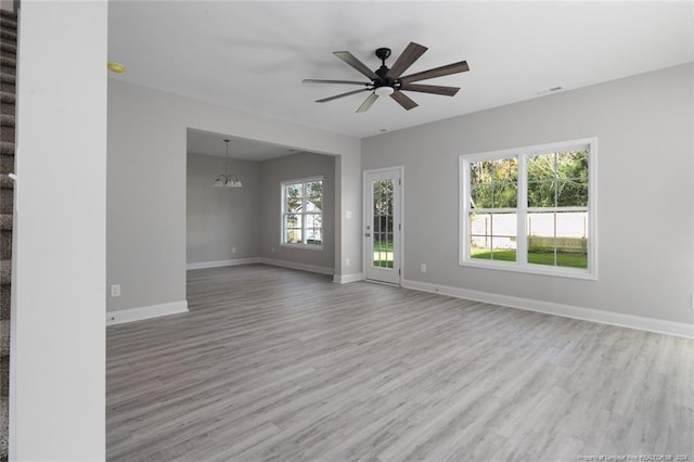 empty room featuring ceiling fan with notable chandelier and light wood-type flooring