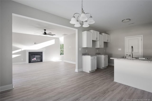 kitchen with sink, pendant lighting, white cabinets, ceiling fan with notable chandelier, and light wood-type flooring