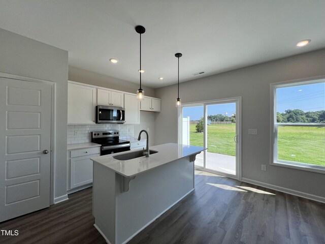 kitchen featuring a kitchen island with sink, sink, appliances with stainless steel finishes, decorative light fixtures, and white cabinetry