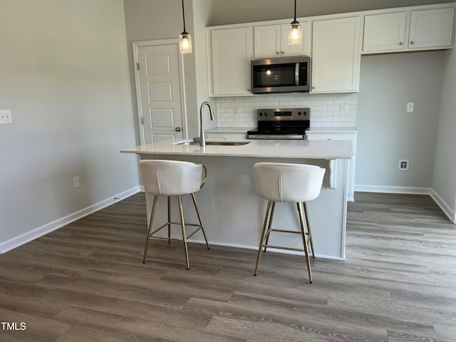 kitchen featuring appliances with stainless steel finishes, sink, decorative light fixtures, white cabinets, and an island with sink