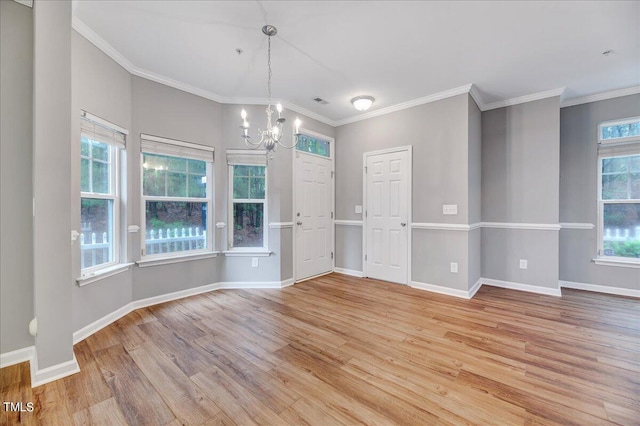 empty room with ornamental molding, an inviting chandelier, and light hardwood / wood-style floors