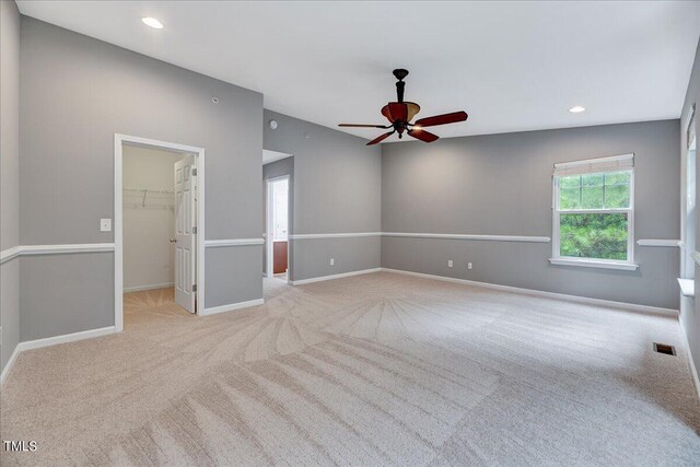 unfurnished bedroom with light carpet, ceiling fan, a closet, and a spacious closet