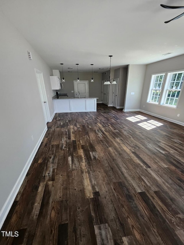 unfurnished living room with an inviting chandelier, sink, and dark hardwood / wood-style floors