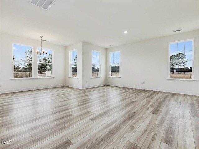 unfurnished living room featuring a notable chandelier, a wealth of natural light, and light hardwood / wood-style flooring