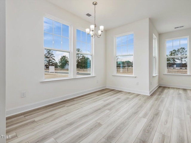 unfurnished dining area featuring plenty of natural light, light hardwood / wood-style flooring, and an inviting chandelier