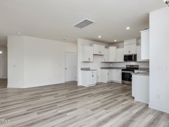 kitchen featuring light stone counters, white cabinets, appliances with stainless steel finishes, and light wood-type flooring