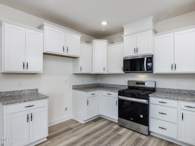 kitchen with appliances with stainless steel finishes, light stone counters, white cabinetry, and light hardwood / wood-style flooring