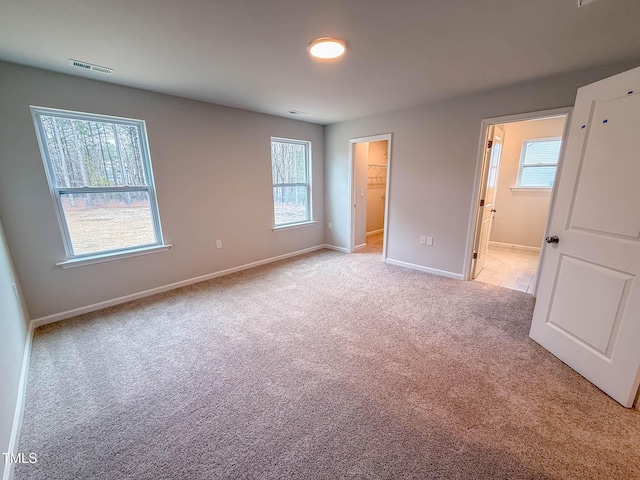 unfurnished bedroom featuring a walk in closet, light colored carpet, ensuite bath, and a closet